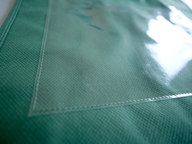 外観ではなく内部業務用に特化した、大きな透明ポケットが特徴の不織布角底手提げ袋。